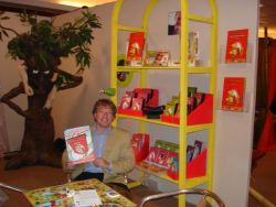Stephan Dunweg, legal advisor, showing off the Alfred J. Kwak - Jouw vriend voor het leven DVDs in a Disky stand on a fair. The folder he's holding says "Net uitgekomen" (lit. "Just released" or "Just hatched"). Several of the marketing flyers can be seen on the stand.